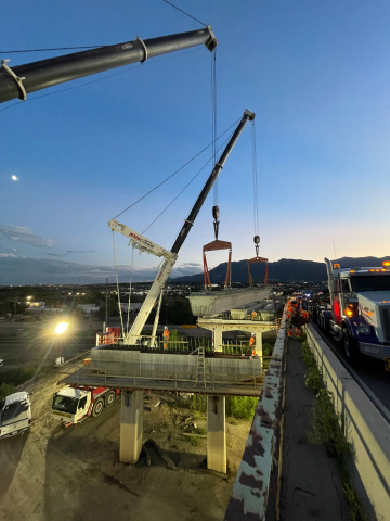 Two cranes work together to place a beam on the Circle Dr. bridge in the early evening