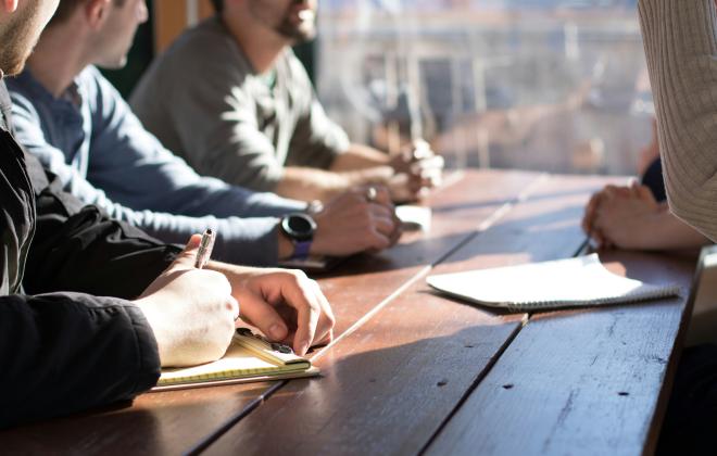 four white people at a table, talking and writing