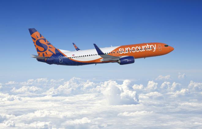 Orange, blue and white plane flying in blue sky above fluffy white clouds